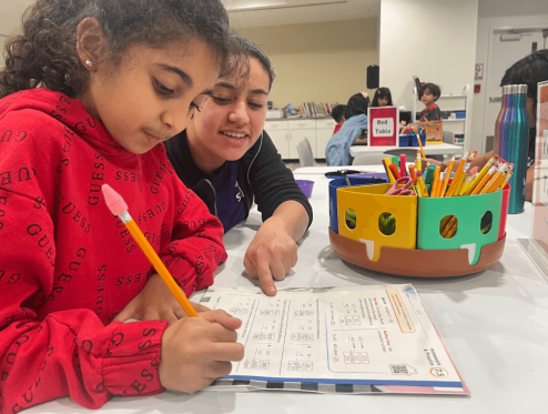 a woman and a girl sitting at a table doing homework