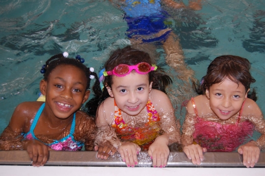 three children in a swimming pool with their arms around the edge of the pool